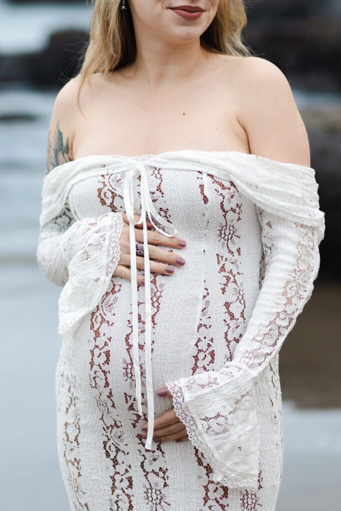 Pregnant mother frames her belly with her hands during maternity photoshoot at the beach.
