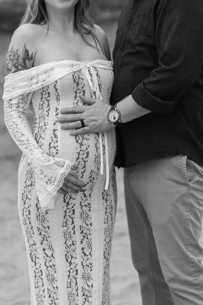 Black and white close up portrait of couples hands on wife's pregnant belly.