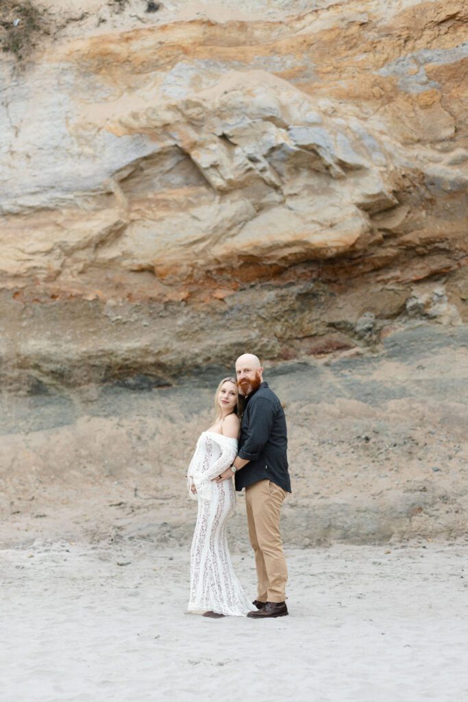Couple stands with rock formation behind them while posing for maternity photos, Portland.