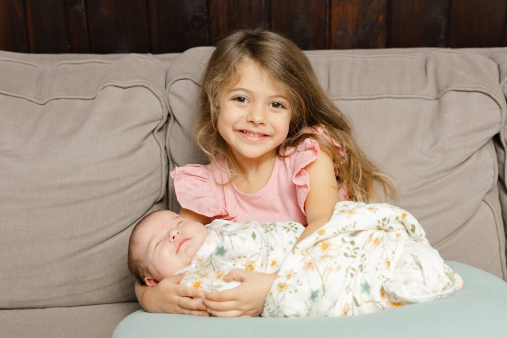 Swaddled newborn baby and with big sister for their first portrait together.