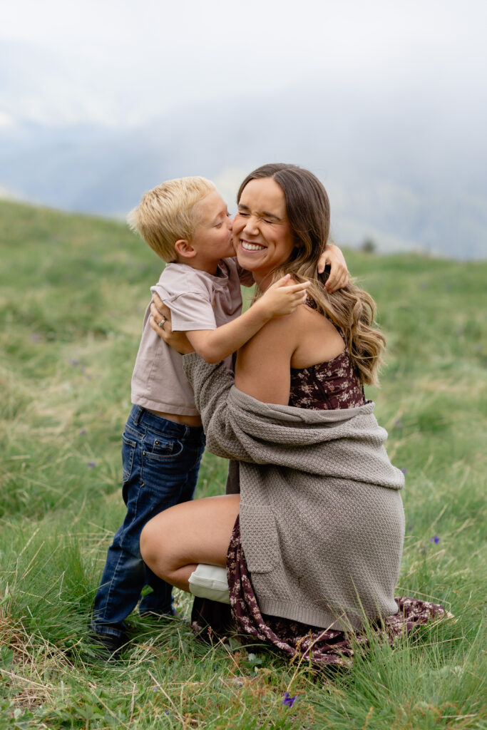 Mom laughs while her little boy kisses her cheek during family portraits.