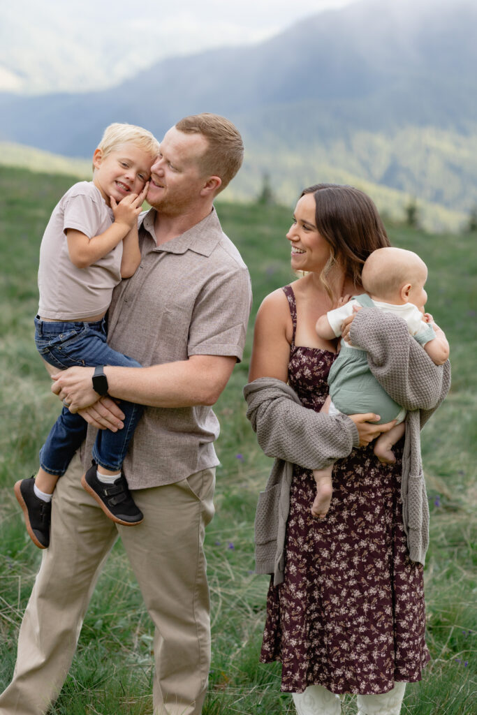 Family in mountains for a photoshoot with parents holding and interacting candidly with their children.