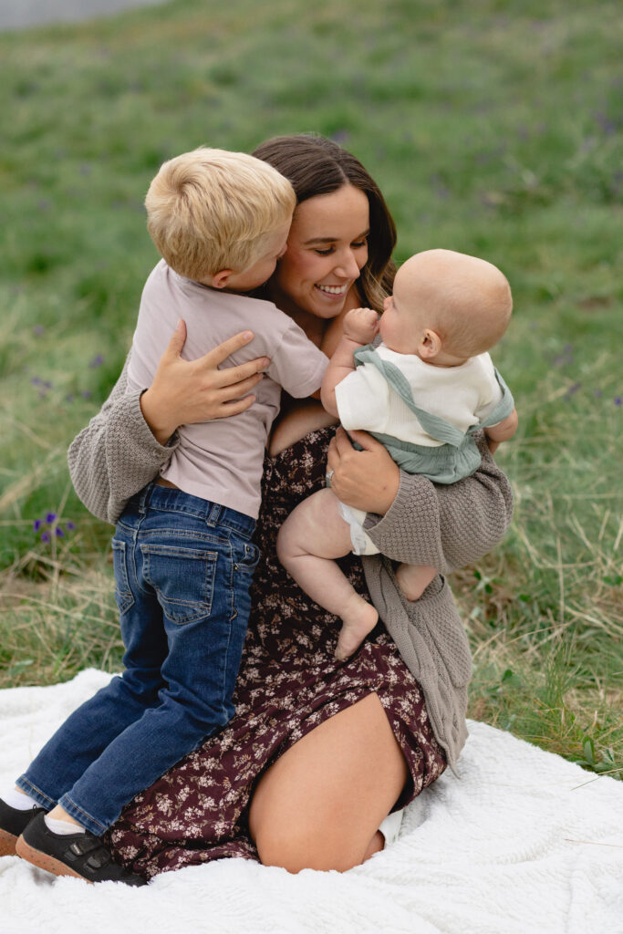 A mom of two boys smiles, holding them close while kneeling on a blanket for a family photos, Portland.