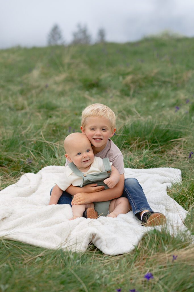 Older brother and younger brother sit together on blanket for family photos, Portland.