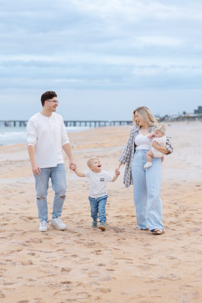 Family of four walk down the beach holding hands and laughing for this Portland lifestyle family photographer's portrait session.