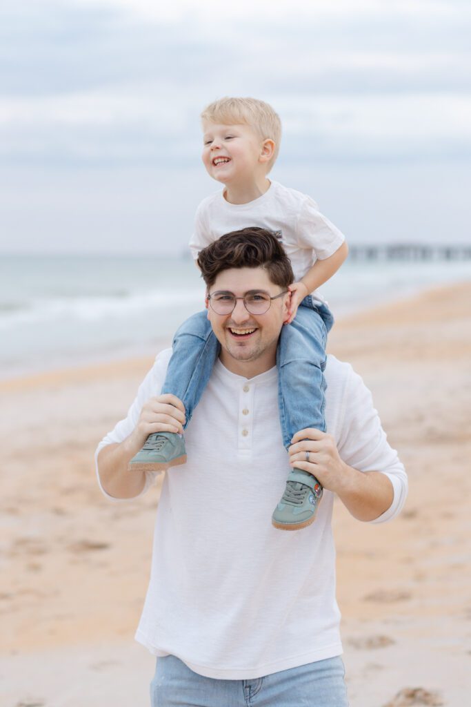 Young boy laughs while sitting on top of his dad's shoulder's during this Portland lifestyle family photographer's beach session.