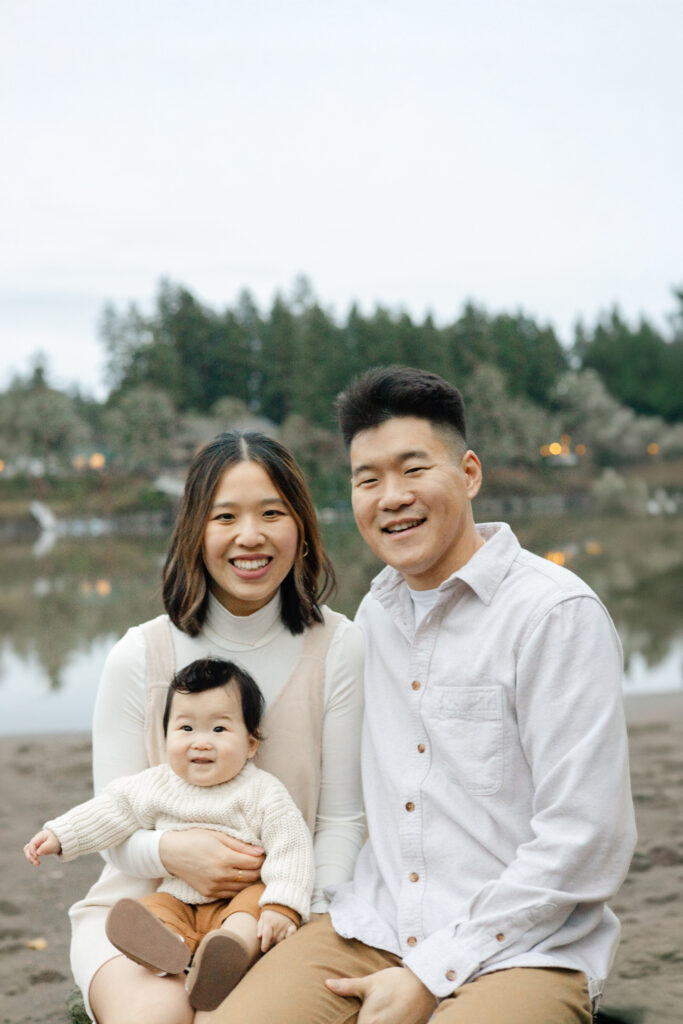 Family of three smile for a seated portrait along the willamette river in Oregon.