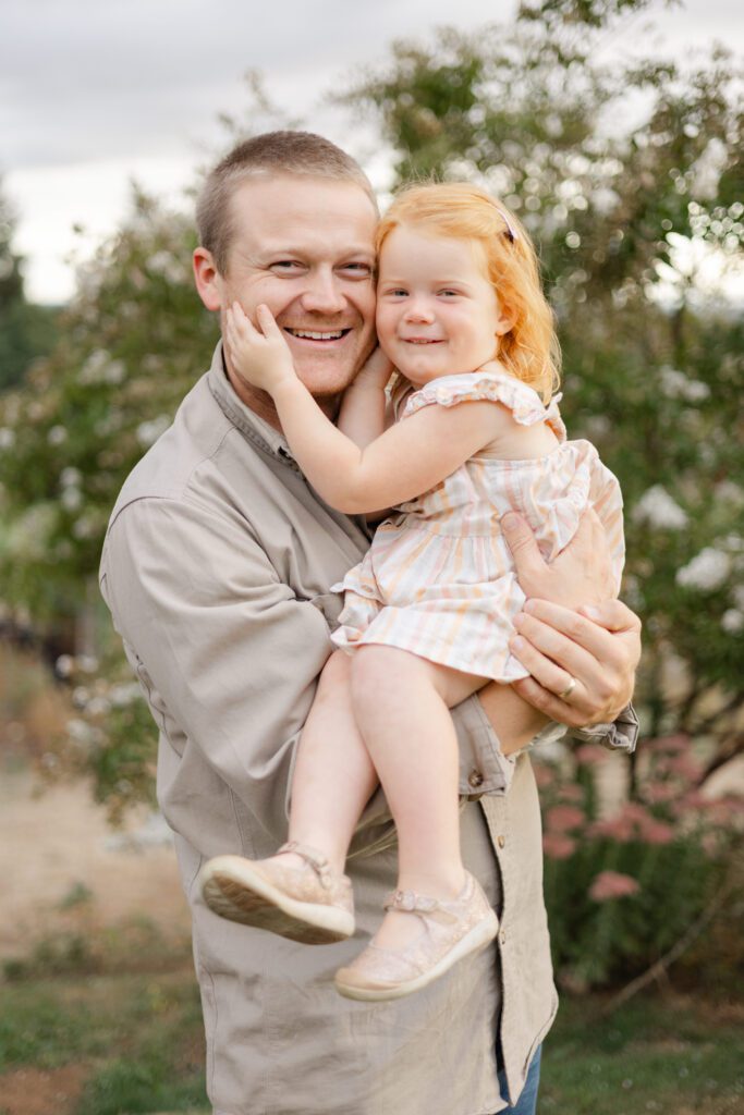 Portland lifestyle family photographer captures daughter cupping her father's face while smiling at the camera.